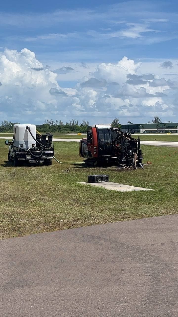 Directional drill and vacuum trailer staged beside a runway for an airfield conduit bore