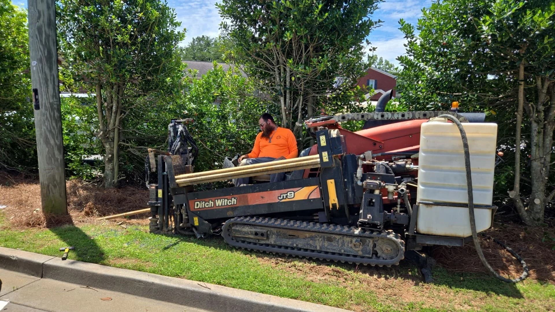 Operator running a Ditch Witch JT9 directional boring rig from a grass strip beside a curb, lawn intact around the rig