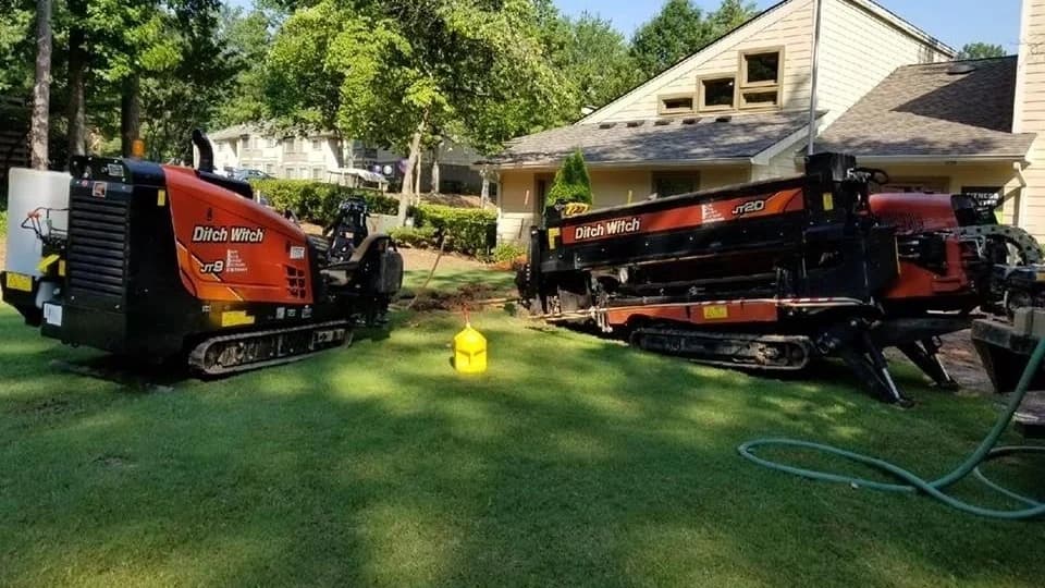 Two Ditch Witch directional drills set up on the lawn of an apartment complex for fiber optic conduit installation without trenching the grounds