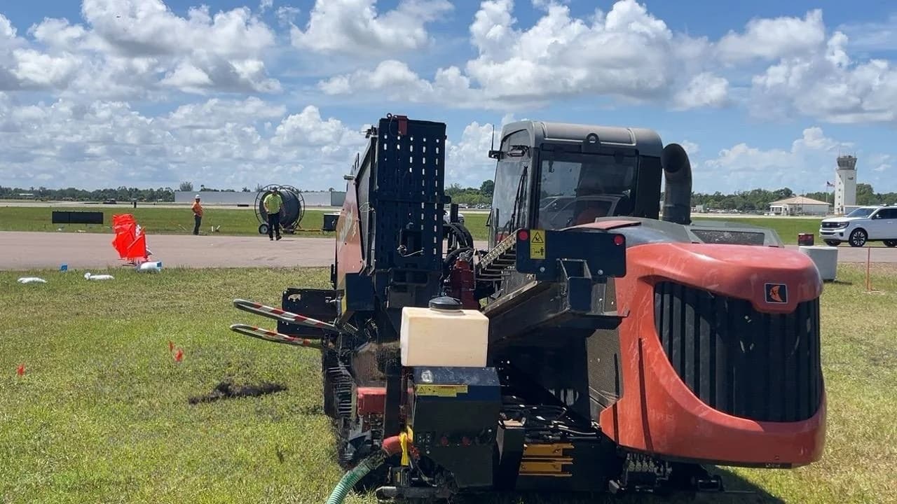 Directional drill on an airfield with a conduit reel and crew in the background, the setup an underground utility contractor brings to a bore